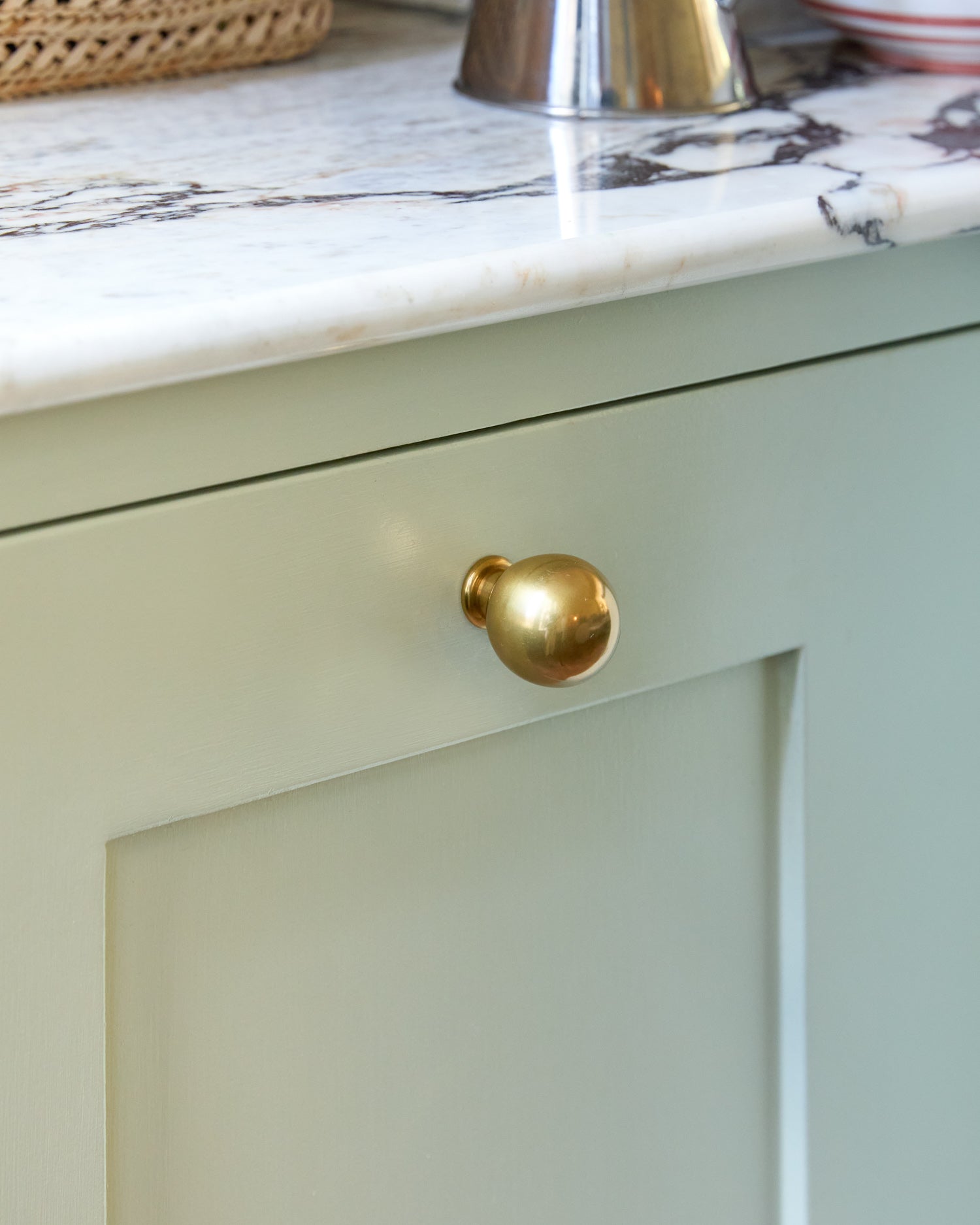 Light green cabinet with a brass knob on a marble countertop